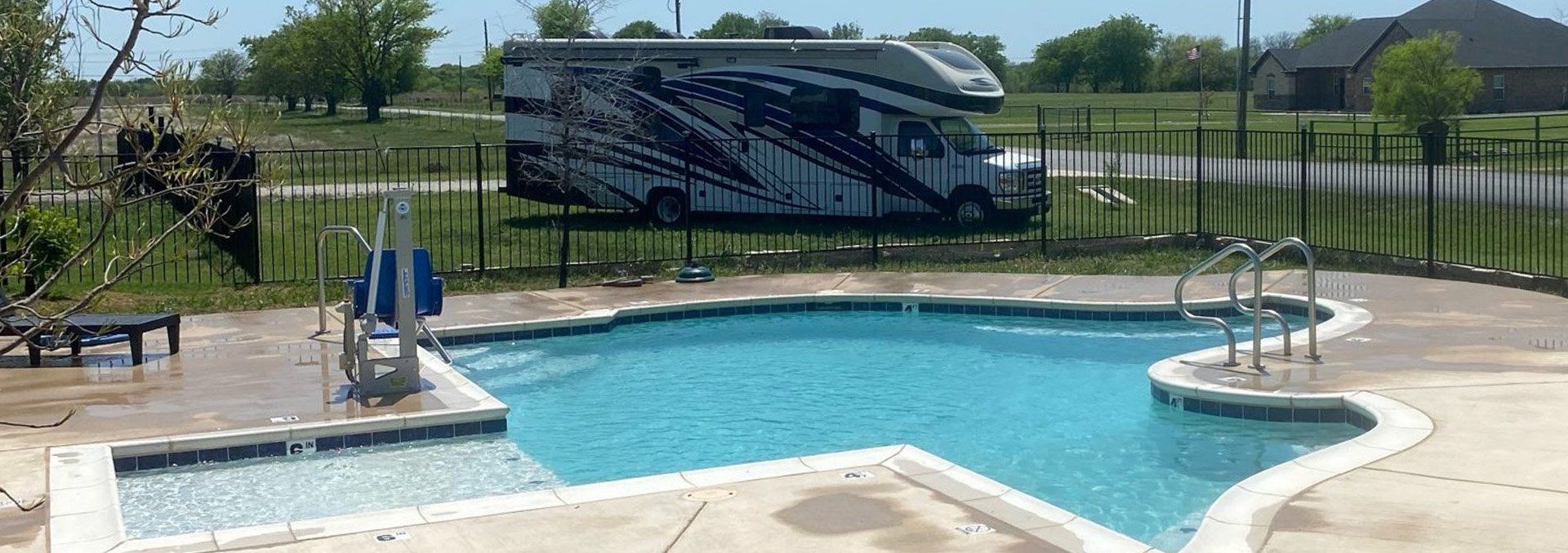 A quirky Texas-shaped swimming pool glistening under bright blue skies at Texas Lakes Ranch RV Park in Aubrey, TX. 